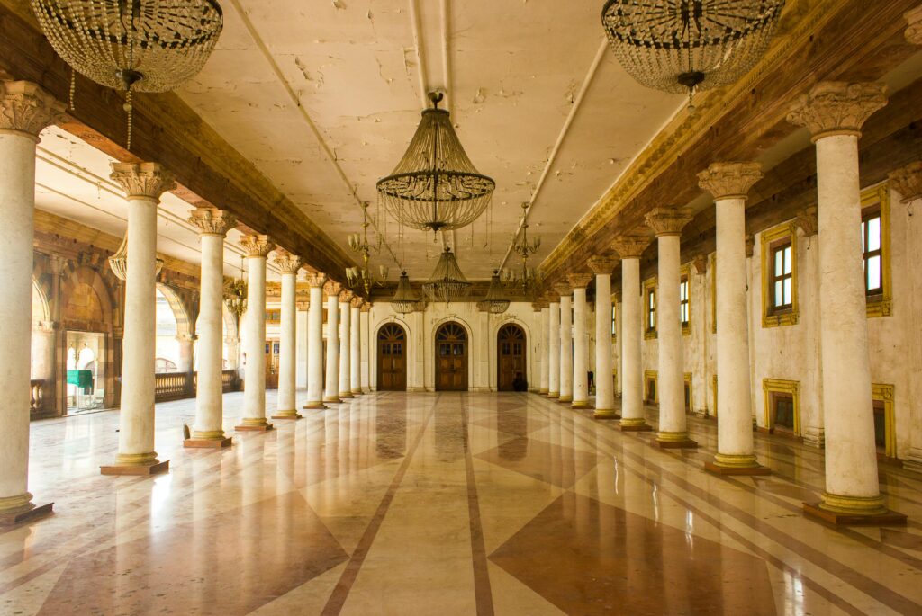 Spacious hall with columns and chandeliers in Rajwada Palace, a historic site in Indore, India.