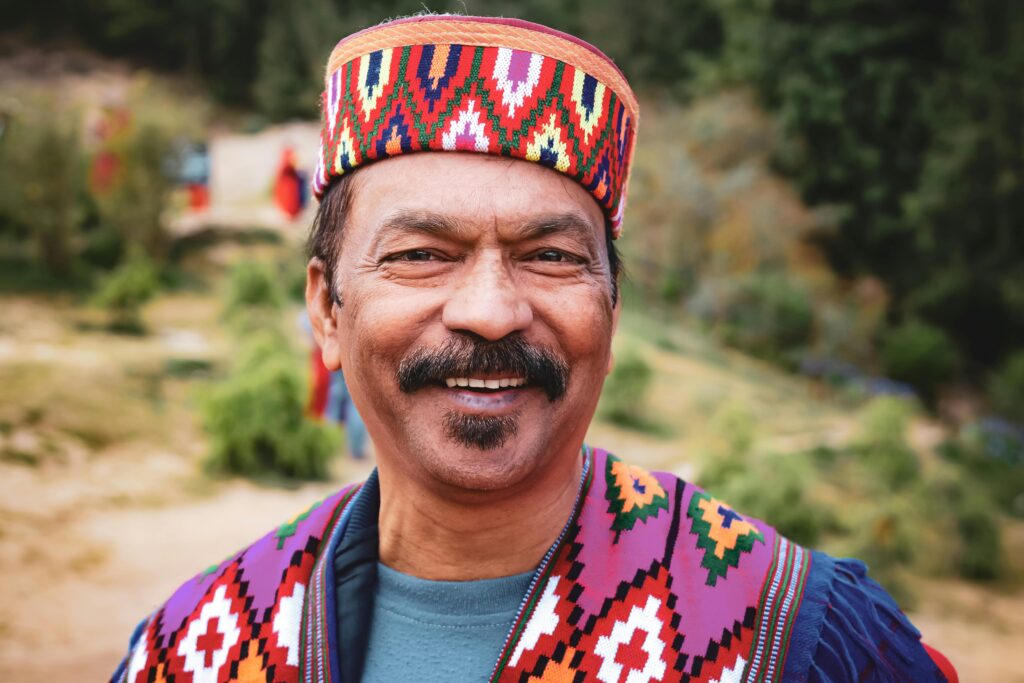Portrait of a smiling man wearing vibrant traditional clothing outdoors in a natural setting.