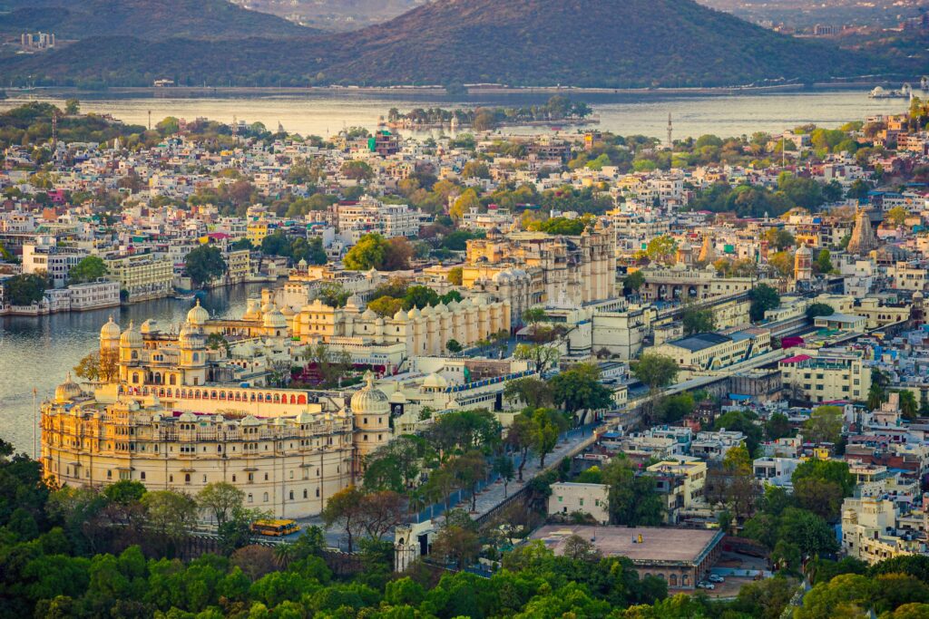 pexels-photo-18526644-18526644 Aerial view of the historic Udaipur City Palace and surrounding cityscape against a tranquil lake backdrop.