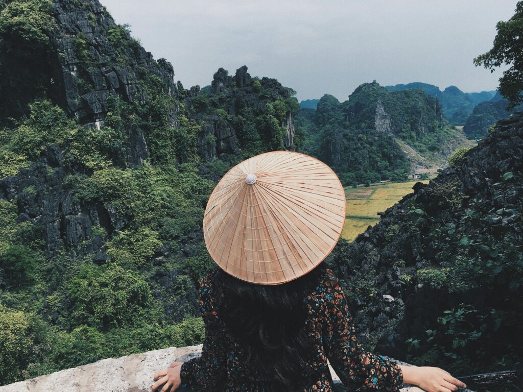 pexels-photo-2602490-2602490 Woman in traditional hat overlooks stunning limestone cliffs in Ninh Binh, Vietnam.