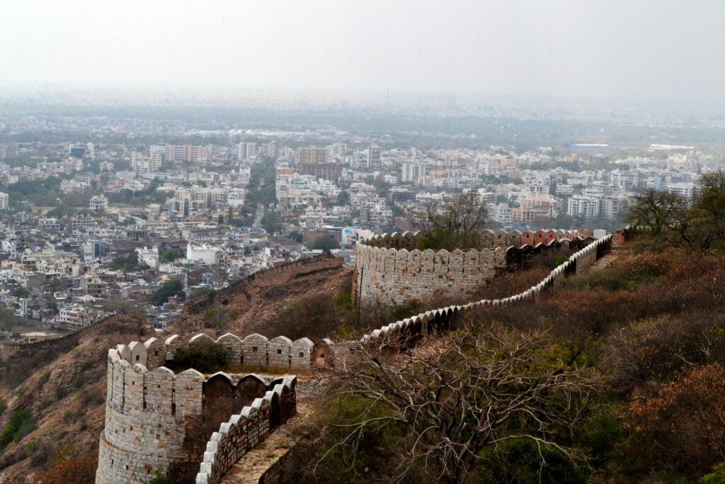 Panoramic view of Jaipur city and historic fort walls from a hilltop location, showcasing urban and natural contrast.