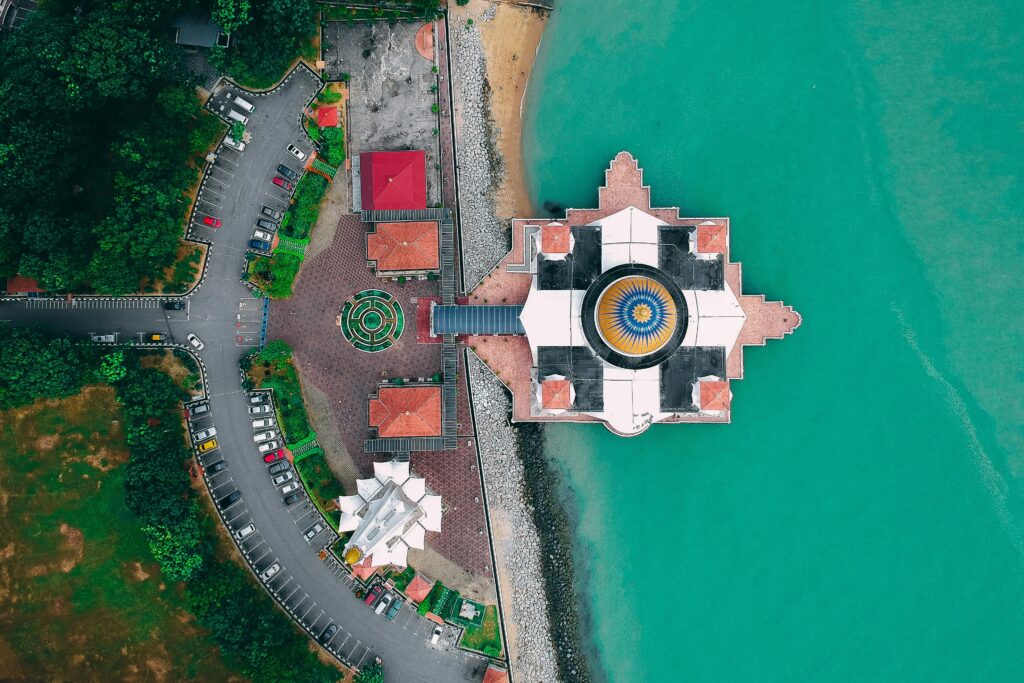 A stunning aerial view of the Melaka Straits Mosque surrounded by turquoise waters and lush greenery.