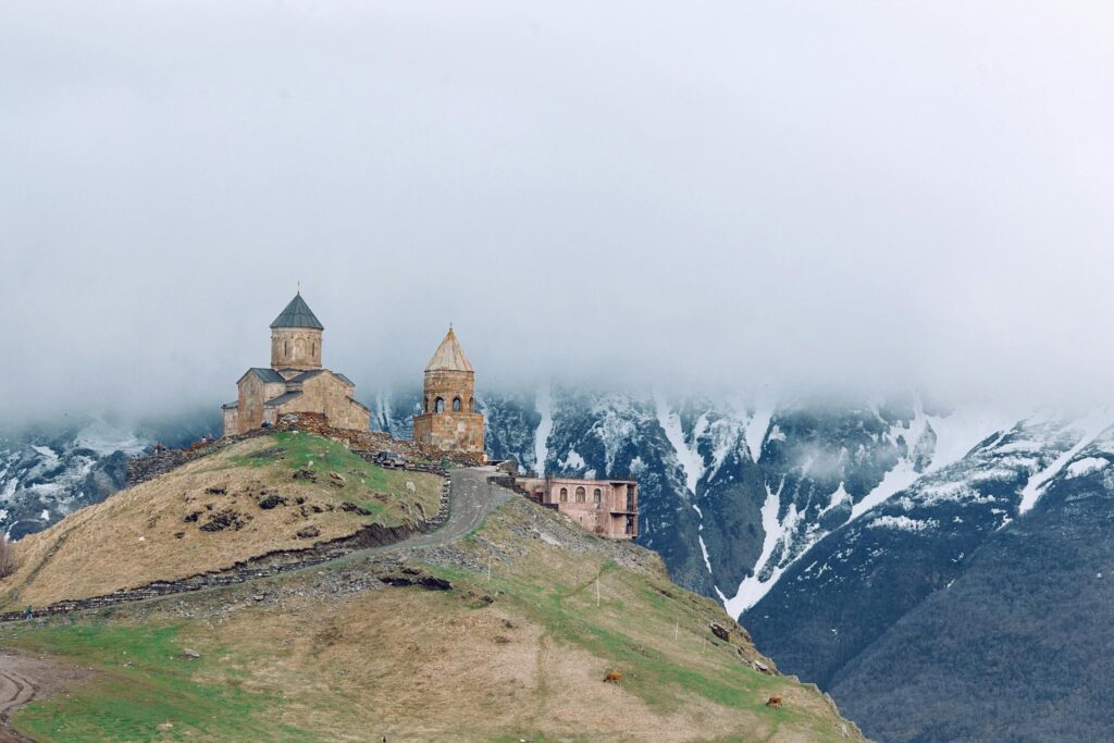 Gergeti Trinity Church atop a hill, shrouded in mist against mountainous backdrop.