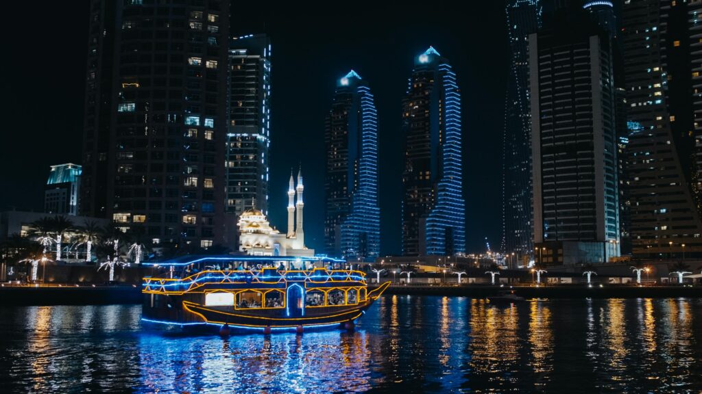 pexels-photo-5087055-5087055 Stunning Dubai marina skyline at night with illuminated buildings and cruise boat on the water.