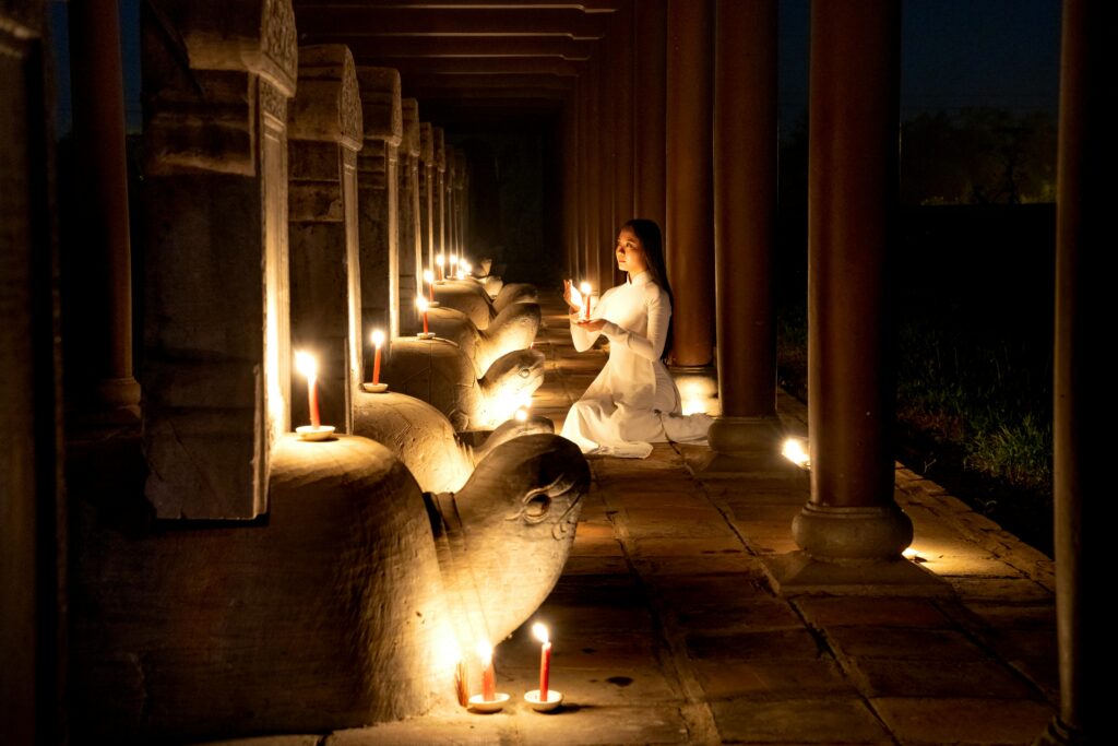 pexels-photo-6710712-6710712 Side view of tranquil Asian female with burning candle in hands praying near stone turtles with steles in dark time