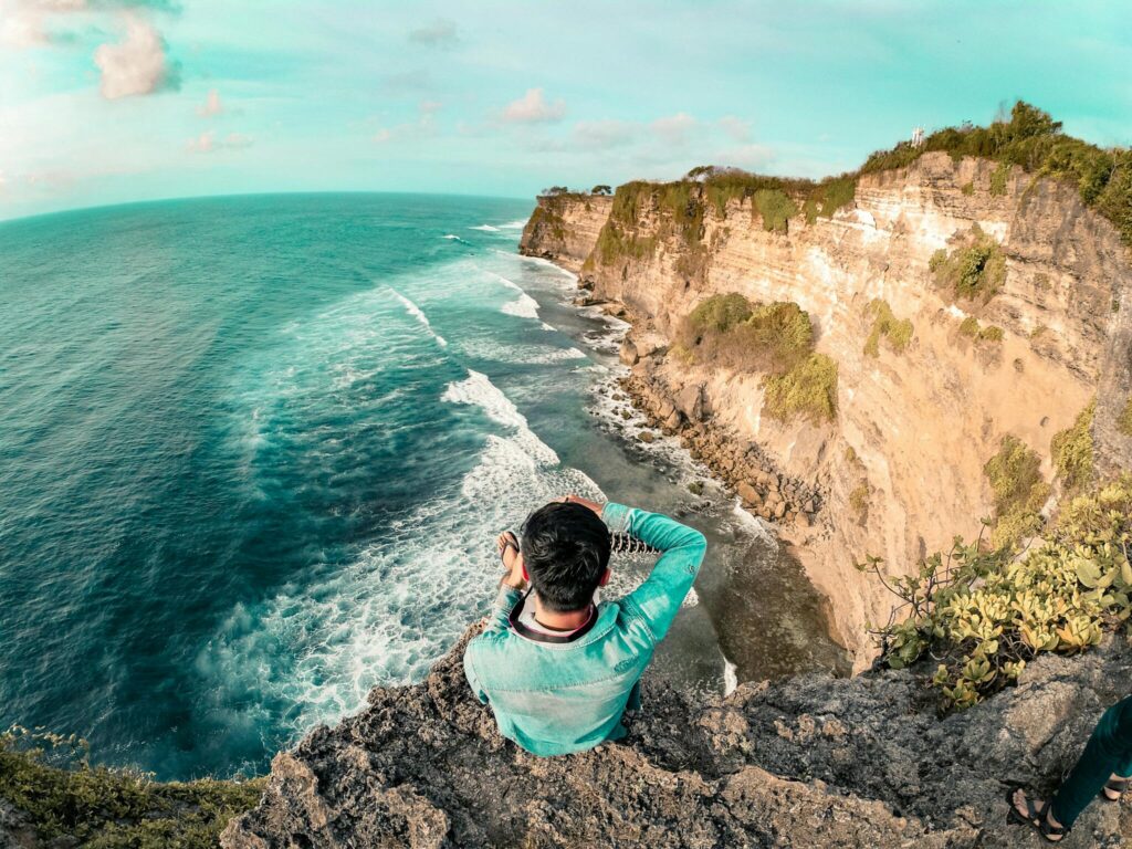 pexels-photo-695782-695782 Man sitting on a cliff edge enjoying the ocean view in Bali. Perfect for travel and relaxation themes.